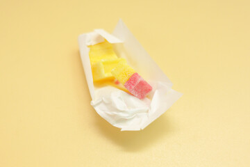 Rectangular yellow and red sugar candies inside a white paper package on orange background. Candy. Yellow. Background. Food. Snack. Sweet. Confectionery. Orange. Sugar. Unhygienic. Bad. Sweets. Flavor