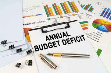 On the table among financial graphs and charts lies a tablet with the inscription - annual budget deficit