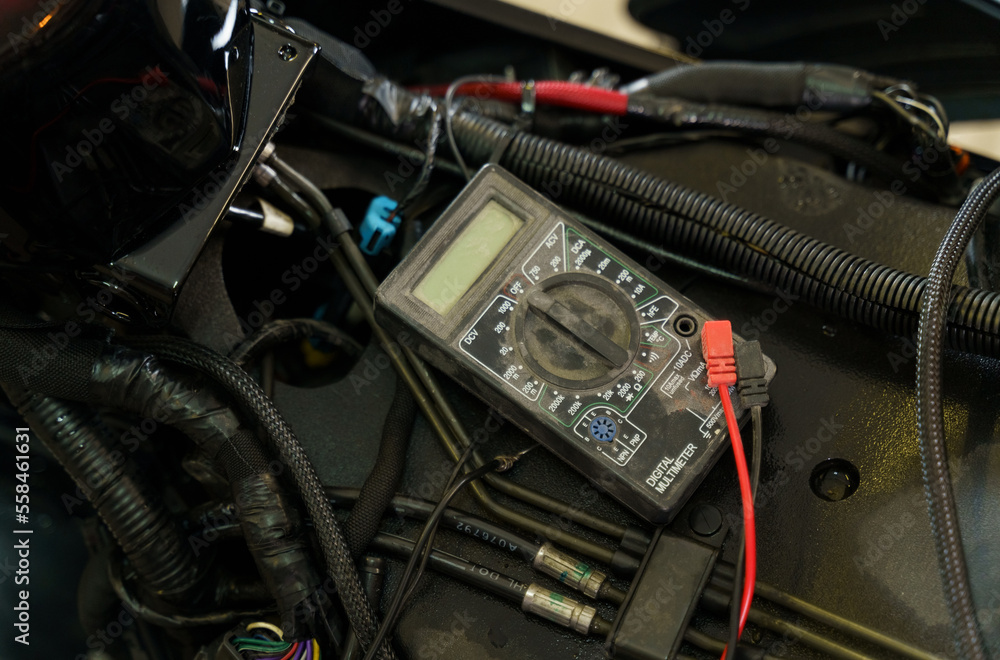 Poster A mechanic using a multimeter checks the voltage level on a motorcycle battery in a garage.