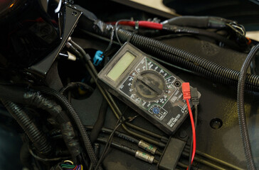 A mechanic using a multimeter checks the voltage level on a motorcycle battery in a garage.