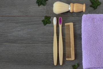 Wooden toothbrushes, bamboo comb, shaving brush, and bathroom towel with green leaves on wooden table. Copy space, top view. Eco-friendly and sustainable hygiene products, plastic-free concept.
