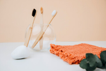 Wooden, bamboo toothbrushes in a glass round vase and orange towel on a white background. Front view
