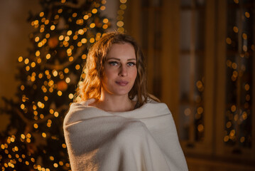 Sexy brown-haired girl in a short silvery dress near the New Year tree in a decorated Christmas...