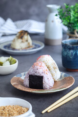 A plate of traditional Japanese rice ball (Onigiri) with chopsticks. Cup of tea in background with fresh vegetables and grilled white sesame. It made from white rice formed into triangular
