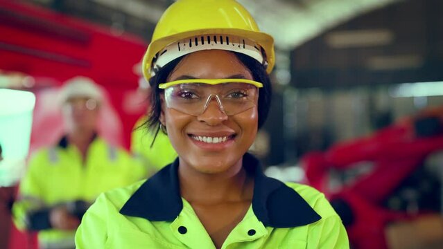 Portrait of woman looking camera at manufacturing special facility. Attractive women industrial engineer wear safety helmet, processes orders and products at manufacturing plant then look at camera.