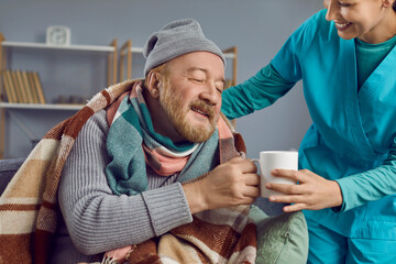 Nurse helping and taking care of a sick senior man. Happy retired old bearded man in a warm blanket...