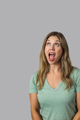 An attractive brunette woman in her forties wearing at shirt looking up with her mouth open in surprise against a gray backdrop