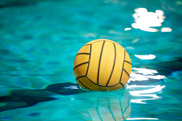 Yellow water polo ball in a swimming pool on blue water background. Film noise and gain - 558485838