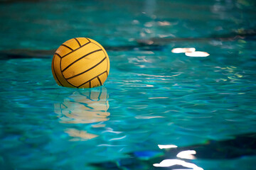 Yellow water polo ball in a swimming pool on blue water background. Film noise and gain - 558486068