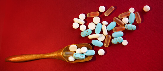 Fototapeta na wymiar The tablets lie in a measuring wooden spoon and are scattered on a red background. The concept of healthcare and medicine.