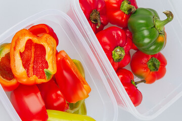 Mixed organic red, green and yellow peppers in a container. Storage of vegetables. Organization of space in the kitchen.