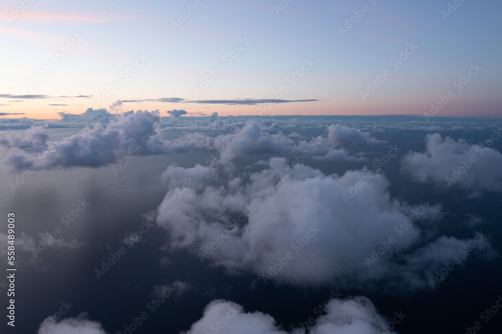 Poster a view of the sky from an airplane window with clouds in the foreground and a plane wing in the dist