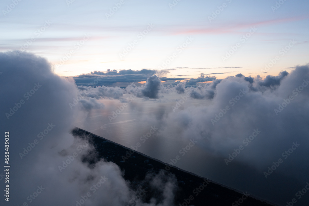 Poster a view of the sky from a plane window with clouds and a plane wing in the foreground and a body of w
