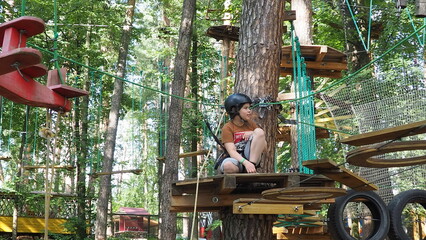 Portrait of cute little boy walk on a rope bridge in an adventure rope park. Child in forest...