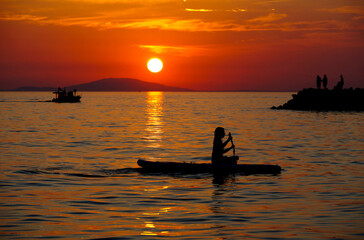Summer activities at sea, fishing, boating and floating on the sup board at the time of the red summer sunset