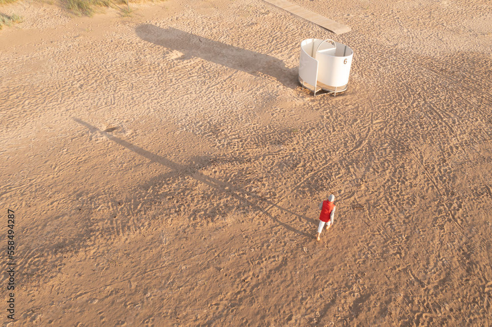 Poster a person standing in the middle of a dirt field next to a white pole and a white bucket on a pole an