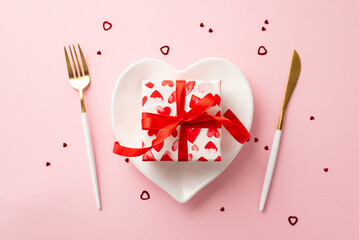 St Valentine's Day concept. Top view photo of heart shaped dish with stylish giftbox knife fork and confetti on isolated pastel pink background