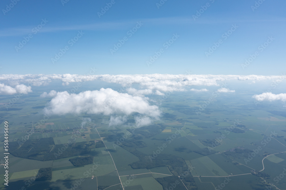 Poster a view of the sky and clouds from a plane window with a view of the land below and the clouds in the