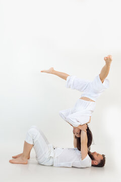 Sporty family on white background. Middle-aged man lying on floor holding young woman stretching legs, practicing yoga.
