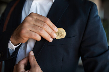 Male ceo manager in suit putting bitcoin coin in pocket, standing in office interior, closeup, cropped