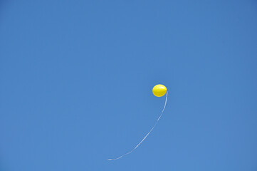 Single yellow balloon flown away in the blue sky background 