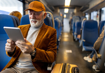 Senior man reading on tablet in train - 558502411