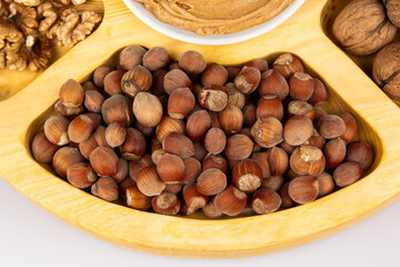 Obraz premium Peanuts, walnuts and hazelnuts in a wooden box with compartments. Three different types of nuts, shelled and shelled, decorative assortment and ready to eat. Closeup, isolated, from above.