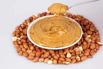 Creamy peanut butter, peanut butter in an open glass jar in the center of a peanut food background. Peanuts in shell, peeled peanuts on a white background. Vegan food concept. Creamy peanut