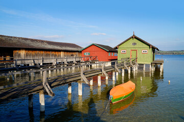Fototapeta premium a long wooden pier leading to the colorful boat houses on lake Ammersee in the German fishing village Schondorf (Ammersee, Germany) 