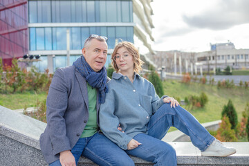 Portrait of amazing family of middle-aged man and young teenage girl sitting on concrete parapet...