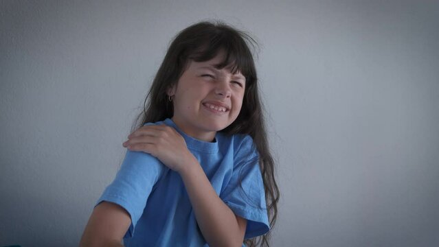 Child feel the pain in arm. A little girl with upset expresion feel the muscles tension in her arm and suffer from pain in the room.