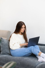  An attractive freelance woman is sitting on the couch and using a laptop to work online. 