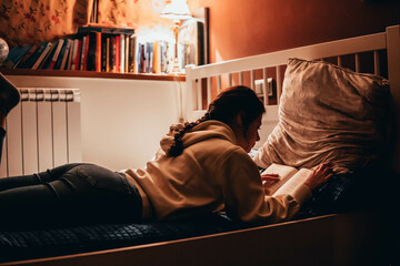 woman reading a book lying in bed at night
