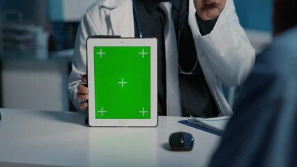Practitioner doctor holding tablet computer pointing at green screen chroma key mock up display explaining medical expertise. Medic and nurse working over hours during checkup visit appointment.