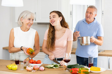 Happy smiling parents enjoy weekend cook with adult daughter in kitchen