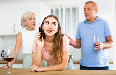 Elderly parents eavesdrop on the phone conversation of their adult daughter in the kitchen
