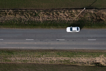 a white car driving down a road next to a field of green grass and a field of brown and green grass...