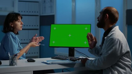 Nurse and physician discussing patient expertise analyzing disease diagnosis report on computer with green screen display. Medical staff working late at night in hospital office, health care service