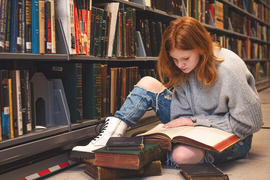 Teen girl sitting on the floor reading in library.