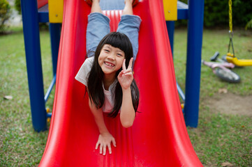 Fototapeta na wymiar Children playing at the playground, happy girl playing slides