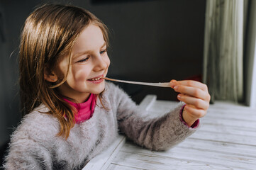 Obraz premium A beautiful smiling red-haired girl, a child chews a sweet chewing gum and stretches it with his hand. Photography, portrait.