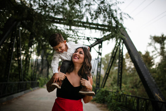 Cheerful mother carrying son on shoulders at bridge