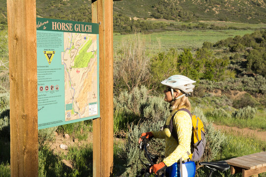 A Woman Reading The Trail Sign While Mountain Biking On The Horse Gulch Trail System, Durango, Colorado