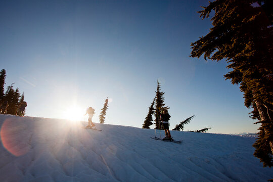Skiers skin up a snowy ridge at sunrise on a blue bird day.