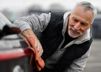 Close-up portrait confident senior man, driver using microfiber cloth, wiping headlights of his car