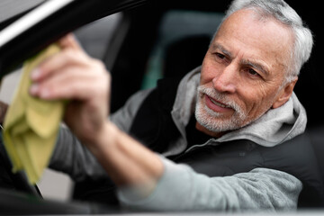 Close-up portrait of handsome positive white-bearded man driver, wiping the car's side mirror