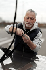 Vertical lifestyle portrait of senior man replacing windshield wipers blades on dealership station. - obrazy, fototapety, plakaty