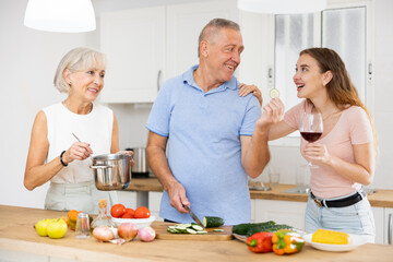 Positive senior couple spending time together with their adult daughter, cooking delicious meals for dinner