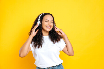 Joyful pretty brunette hispanic woman, in casual basic wear, with headphones, listens her favorite...