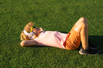 Cute little child listens to music in headphones. Childhood lifestyle concept. Kid enjoy summer music outdoor in park. Kid spends free time with favorite music.